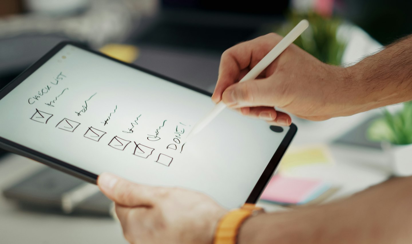 Hands using a stylus to check items on a tablet.